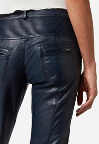 Navy leren broek met een gladde textuur, voorzien van geribbelde details bij de taille en twee achterzakken met ritssluitingen.
