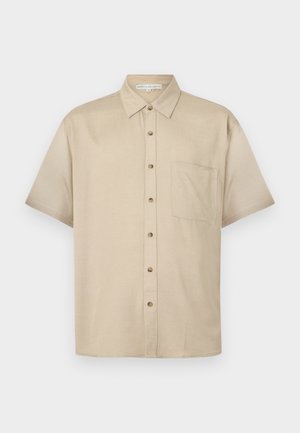 Kortermet, lys beige skjorte laget av myk stoff, med krage, frontknapping og en enkelt brystlomme.