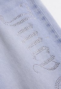 Υφασμα από ανοιχτό μπλε τζιν με λαμπερό σχέδιο από στρας σε γραφή με καλλιγραφικά γράμματα, που παρουσιάζει ομαλή υφή και διακριτική παλαίωση.