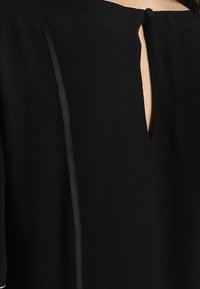 Vestido negro con detalle de abertura en la espalda, textura suave y ribete en contraste a lo largo de las costuras laterales. Diseño sencillo con mangas cortas.