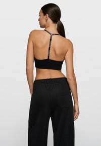 Top deportivo negro con diseño de espalda racer y tirantes con logo, combinado con pantalones de chándal negros de corte holgado que tienen un bolsillo trasero.