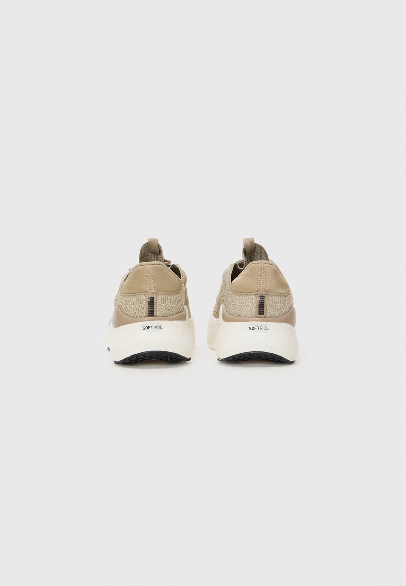 Zapatillas deportivas beige con parte superior de malla de punto y suelas blancas acolchadas. Presentan lengüetas y detalles texturizados en el talón. Adecuadas para un uso casual.