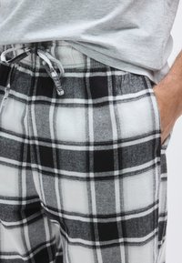 Svart-hvitt rutete loungebukse i mykt stoff med elastisk midjebånd, snor og sidelommer. Sjakkbrettmønster synlig.