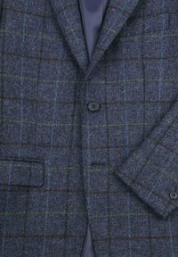 Marineblauwe geruite blazer van een gestructureerde stof, met groene en bruine accenten, een enkele knoopsluiting en een geknipt revers.
