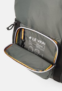 Mochila de nailon ripstop gris con un bolsillo con cremallera. Presenta acentos en naranja y amarillo, y las dimensiones están indicadas en la etiqueta interior.
