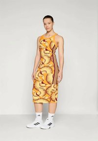 Yellow midi dress with a floral pattern in orange and brown, featuring a racerback design. Paired with white sports socks and shoes.