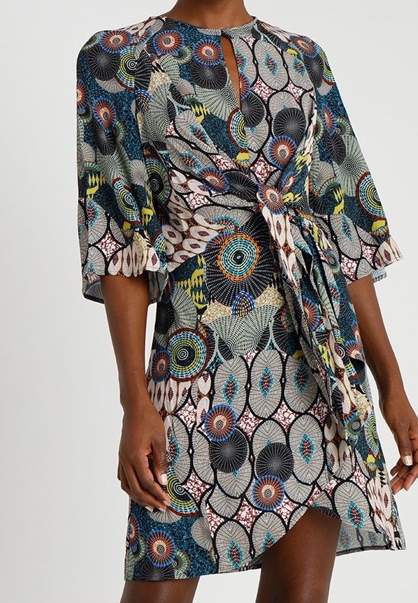 Femme portant une robe longueur genou avec des motifs circulaires et géométriques multicolores et des manches trois-quarts.