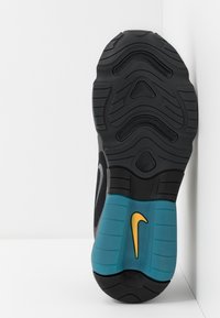 Mustan ja turkoosin värinen Nike-tennarien pohja, jossa on keltainen swoosh-logo ja teksturoitu pito, esitelty valkoista nurkkaa vasten.