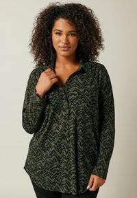 Camisa de manga larga abotonada en verde oscuro con un patrón de zigzag negro, que presenta un cuello con solapa y una tela suave y texturizada.