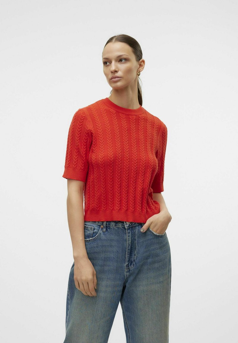 Rød cropped striktrøje med et struktureret kabelmønster og korte ærmer, parret med højtsiddende denim jeans.