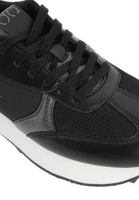 Zapatilla negra que combina cuero y materiales de malla, forma redonda, suela blanca plana y detalles texturizados en los laterales.
