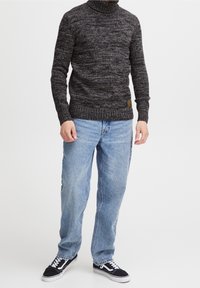 Mörkgrå stickad polotröja med ett strukturerat mönster, kombinerad med ljusblå raka jeans och svarta sneakers med vita detaljer.