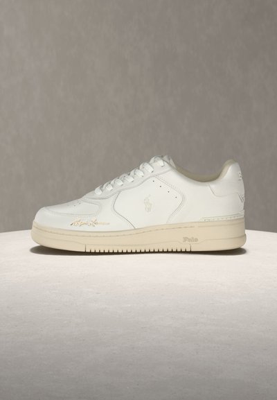 Άσπρο δερμάτινο χαμηλό sneaker με μπεζ σόλα, σχεδίαση με κορδόνια, διακριτικό λογότυπο στο πλάι και χαρακτηριστική λεπτομέρεια κοντά στα δάχτυλα σε ουδέτερο φόντο.