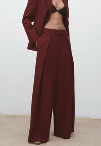 Bordeaux op maat gemaakte blazer en wijde broek, met scherpe plooien en een gladde textuur, gecombineerd met een zwarte bikinitop.