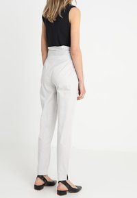 Witte op maat gemaakte broeken met een hoge taille, taps toelopende pijpen en splitten bij de enkel, gecombineerd met een mouwloos zwart topje en zwarte flats.