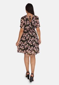 Vestido negro con estampado floral, de mangas cortas y un detalle de lazo en la espalda. Presenta una cintura ajustada y una falda fluida. Patrón floral en tonos rosa y verde.