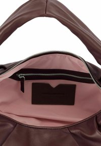 Sac à main en cuir marron avec une texture douce, doté d'un intérieur rose clair, d'une poche zippée et d'une étiquette logo à l'intérieur.