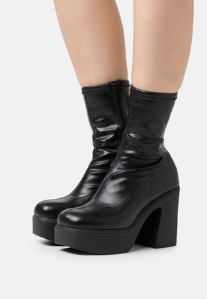 Czarne botki na platformie z ekoskóry z wysokim obcasem w kształcie słupka, charakteryzujące się eleganckim wzornictwem i zapięciem na zamek. Gładka tekstura i dopasowana cholewka.