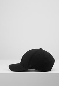 Svart baseball cap laget av stoff med en buet skygge, med en brodert logo foran og en subtil merkevaretag på siden.