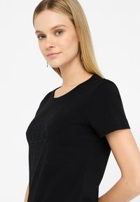 T-shirt nera a maniche corte con un motivo testurizzato di punti e linee sul davanti. Tessuto di cotone morbido. Collo rotondo.