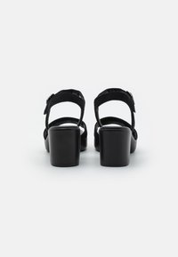 Sandali neri in suede con tacco a blocco, aperti sul retro e con cinturino alla caviglia regolabile. Tessuto liscio e design del tacco robusto per il supporto.
