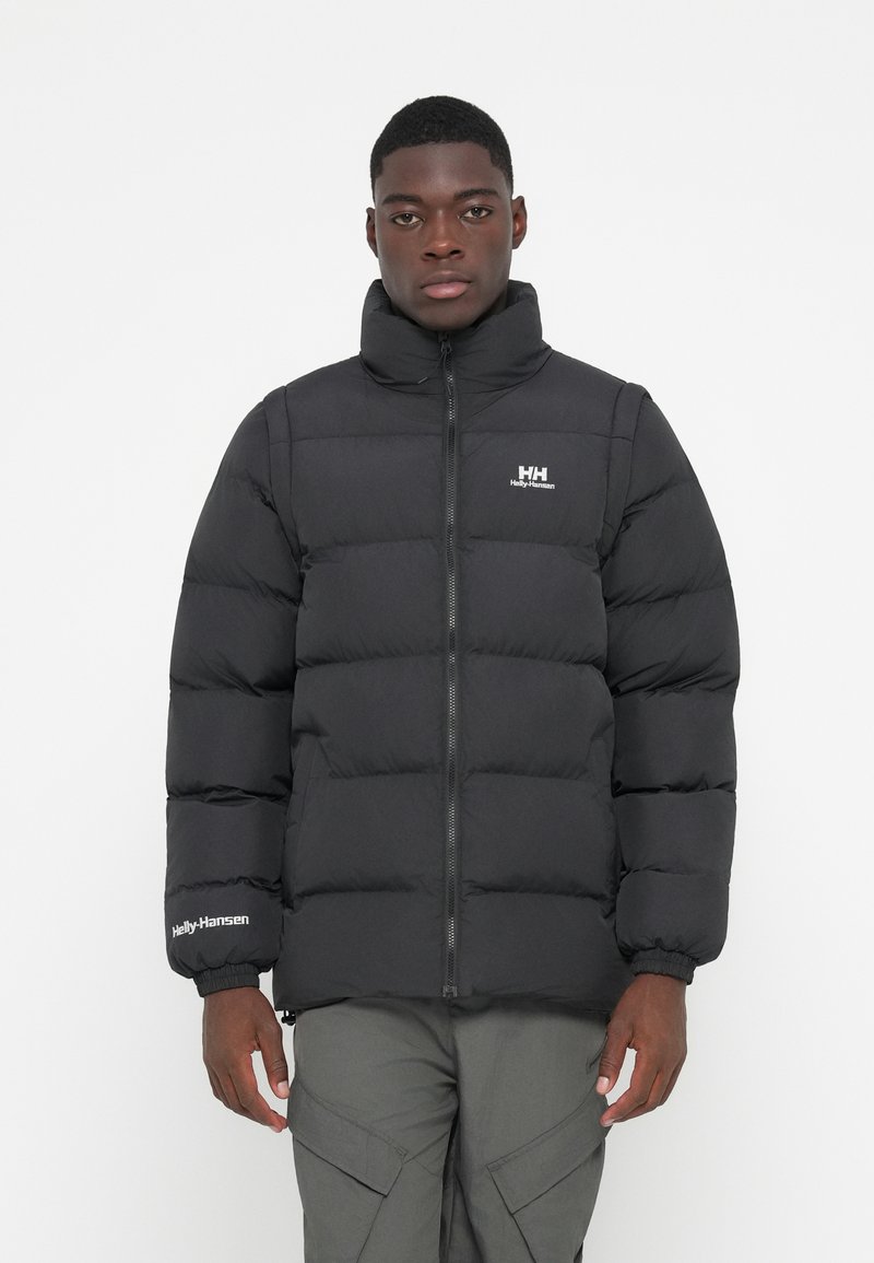 Veste matelassée noire avec col montant, fermeture éclair à l'avant et poignets élastiques. Présente le logo "Helly Hansen" sur la poitrine et la manche.