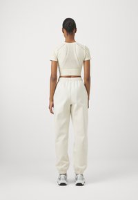 Kremfarget cropped topp med meshdetaljer, kombinert med kremfargede joggebukser med elastisk midje og samlet mansjett. Treningser sko fullfører antrekket.