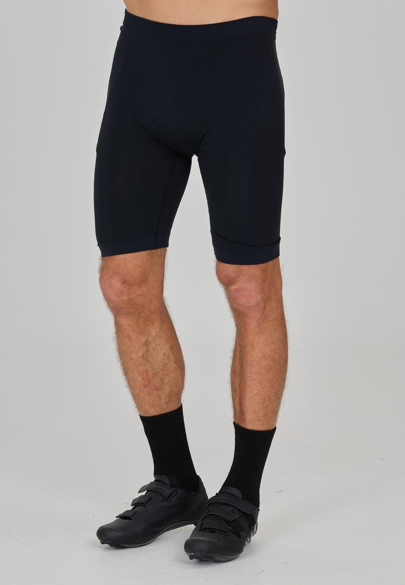 Zwarte sportshorts van rekbaar materiaal, met een tailleband en een knielange snit. Draag dit met zwarte fietsschoenen en sokken.