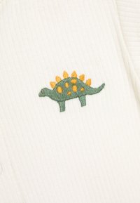 Zielony i żółty wyszywany dinozaur stegozaur na białym żebrowanym materiale.