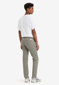 Pantalones de algodón grises con bolsillos laterales y un bolsillo trasero tipo parche, combinados con una camiseta blanca holgada y zapatillas blancas. Diseño minimalista.