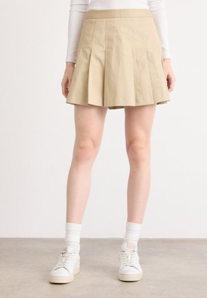 Beige plisseret skjørt laget av glatt stoff, med høy midje og kne-lengde design, stylet med hvite sneakers og sokker.