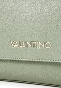 Sac en cuir texturé vert clair avec un logo "Valentino" embossé en doré métallique, agrémenté de coutures le long des bords.