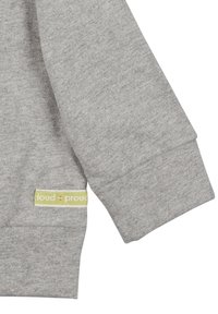Manica in cotone grigio con polsino a coste e etichetta verde con il logo "loud + proud". Texture morbida, design casual.