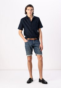 Chemise navy à manches courtes assortie à un short en denim retroussé. Une ceinture en cuir marron et des mocassins noirs complètent le look. Design simple et décontracté.