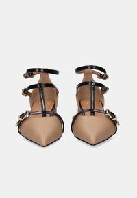 Bailarinas beige de punta con correas de charol negro, con adornos de hebillas en tono dorado y diseño de correa en el tobillo.