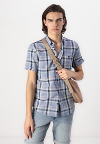 Korte mouwen geruit shirt in blauw met grijze en rode tinten, met een knopenrij en gecombineerd met licht denim shorts en een beige schoudertas.