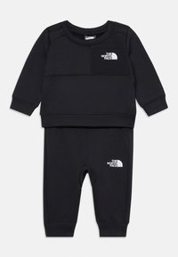 Ensemble noir en deux pièces en tissu doux, comprenant un haut à manches longues avec un petit logo blanc sur la poitrine et un pantalon assorti avec des accents de logo.