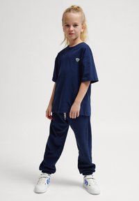 Marineblå kortärmad t-shirt med en broderad design på bröstet, tillsammans med matchande marineblå joggingbyxor och vita sneakers med blå accenter.