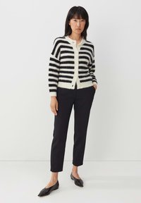 Gestreepte cardigan in zwart en crèmekleur met een zachte textuur, voorzien van een knopenfront en ribgebreide manchetten, gecombineerd met zwarte nauwsluitende broek en ballerina's.