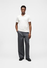 Λευκό πόλο πουκάμισο με γιακά, συνδυασμένο με γκρι παντελόνι φαρδιάς γραμμής και μαύρα παπούτσια. Καθαρός, μινιμαλιστικός σχεδιασμός με ουδέτερα χρώματα.