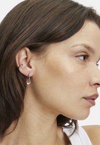 Silberne Creolen werden gezeigt, mit einer runden und tropfenförmigen Form, mit einer polierten Oberfläche und glatter Textur. Einfaches Design.