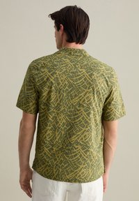 Camicia a maniche corte di colore verde con un motivo astratto giallo chiaro. Presenta un colletto e una vestibilità rilassata, realizzata in tessuto traspirante.