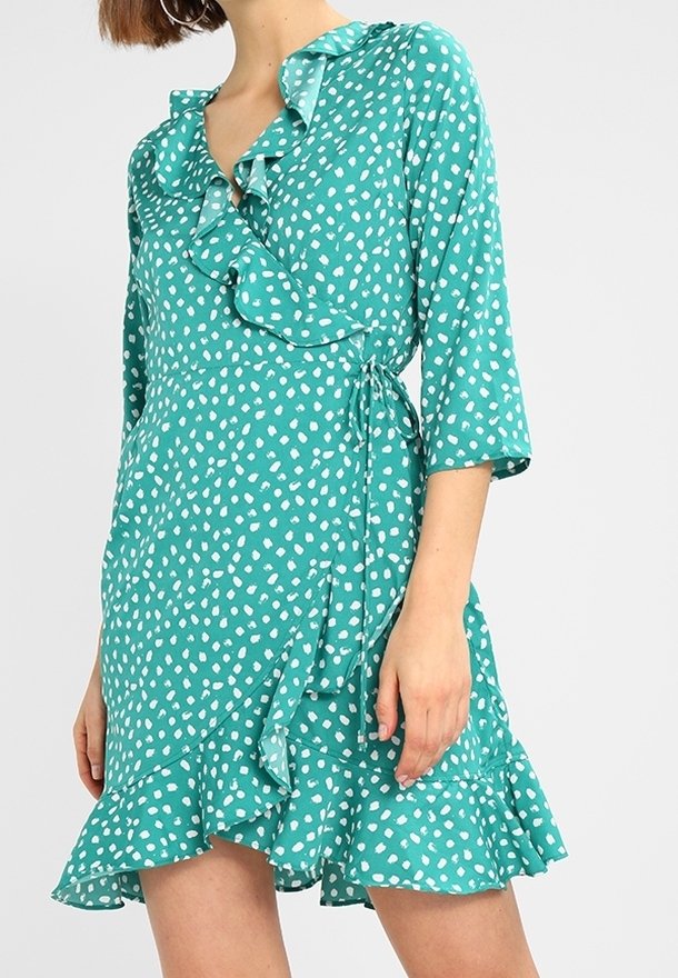 Robe bleu sarcelle à pois blancs, décolleté et ourlet à volants, manches trois-quarts, avec détail de ceinture nouée, fabriquée en tissu léger.