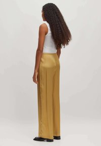 Satin, hochtaillierte, weite Hosen in einem goldgelben Farbton, mit einer glatten Textur und elastischem Bund, kombiniert mit einem taillierten weißen Tanktop.
