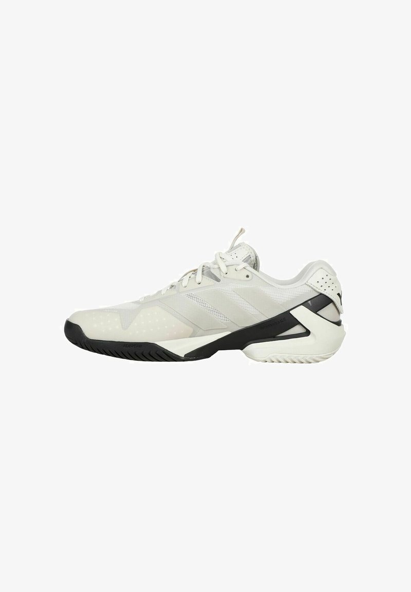 Zapatilla deportiva blanca con materiales de malla y sintéticos, con una suela de goma negra y acentos texturizados. Presenta cordones y detalles del logo.