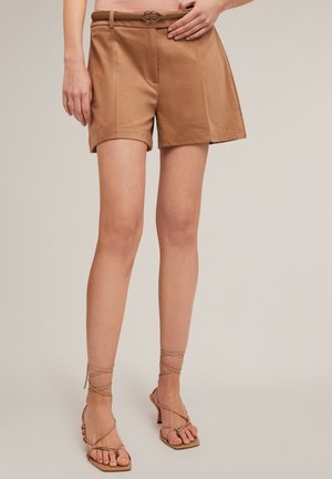 Tan hoge taille shorts met een gladde textuur, zijzakken en een riem met een decoratieve gesp. Gecombineerd met blootkleurige sandaaltjes met bandjes.