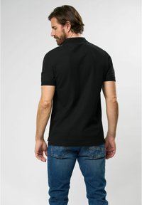 Black polo shirt made of cotton, featuring short sleeves, a classic collar, and a straight hem. Paired with blue denim jeans.