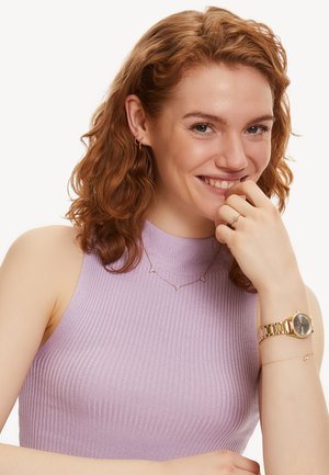Top lilas sans manches en maille côtelée. Boucles d'oreilles en or en forme de créole, collier superposé avec de petites perles, montre en or avec un cadran argenté et un bracelet délicat.