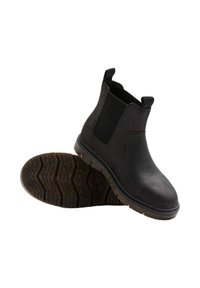 Botas Chelsea negras de tobillo fabricadas en cuero suave, con paneles laterales elásticos, lengüetas y suelas de goma texturizadas con un patrón de zigzag.