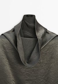 Tissu gris foncé froissé avec un col roulé large et haut plié sur un fond blanc.